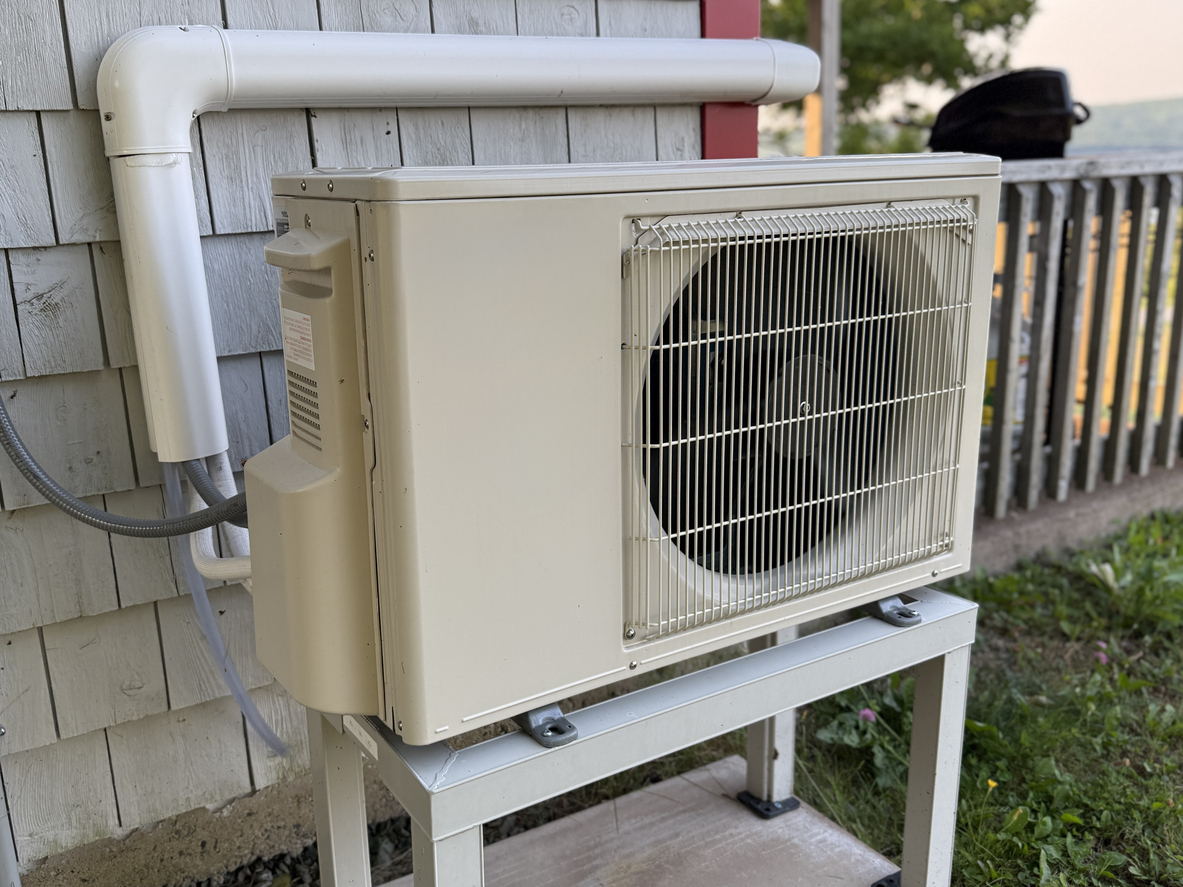 Outdoor heat pump unit on a raised stand beside a Fredericksburg, VA house.